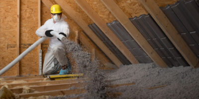 Technician in protective gear applying TAP -pest control insulation in an attic space using specialized equipment