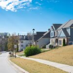 A suburban street in Brunswick, GA features neatly lined, pest-free homes under a clear blue sky. The road slopes gently with a visible 25 mph speed limit sign. Each house boasts well-maintained lawns, and the mostly bare trees hint at late autumn's embrace.